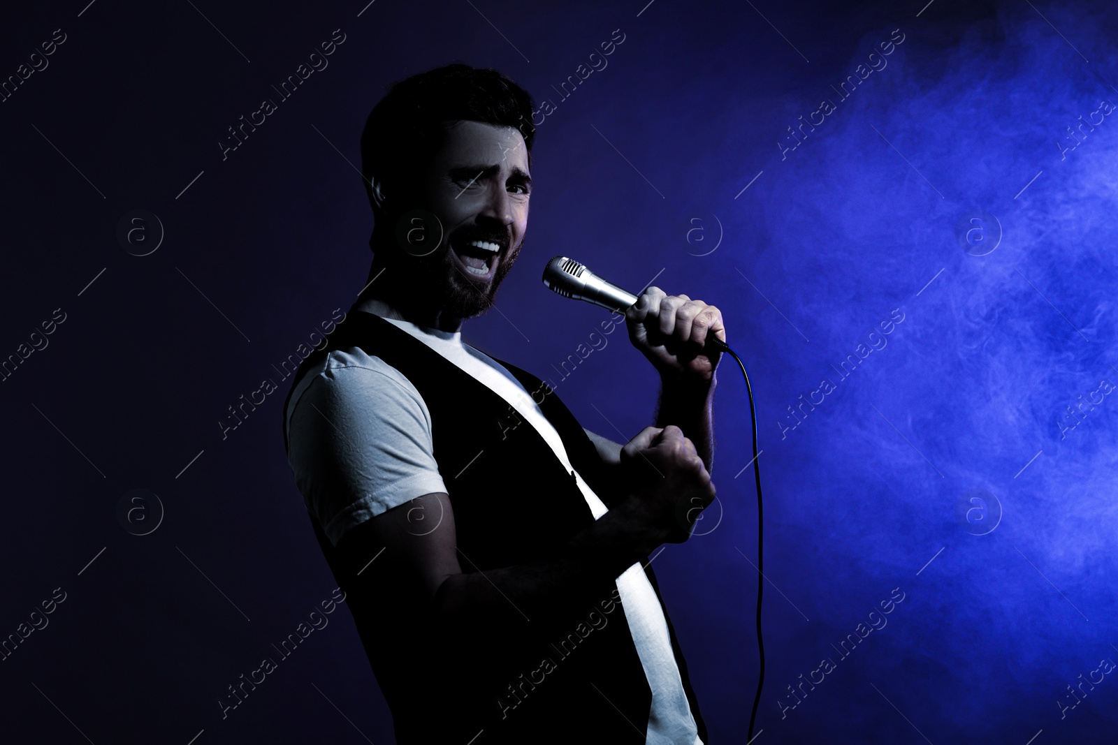 Image of Singer performing on stage. Man with microphone in smoke