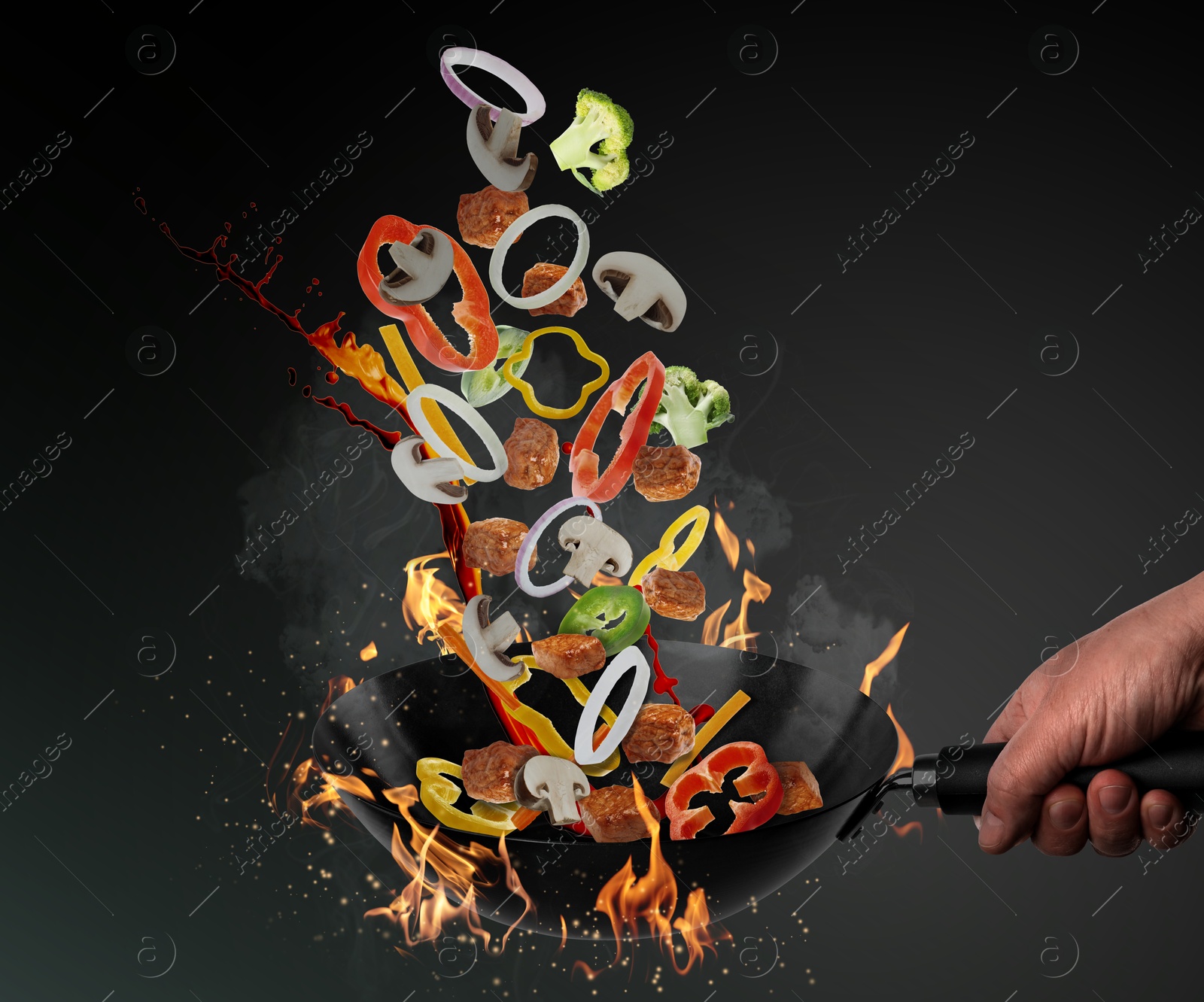 Image of Man tossing ingredients in wok over fire on black background, closeup