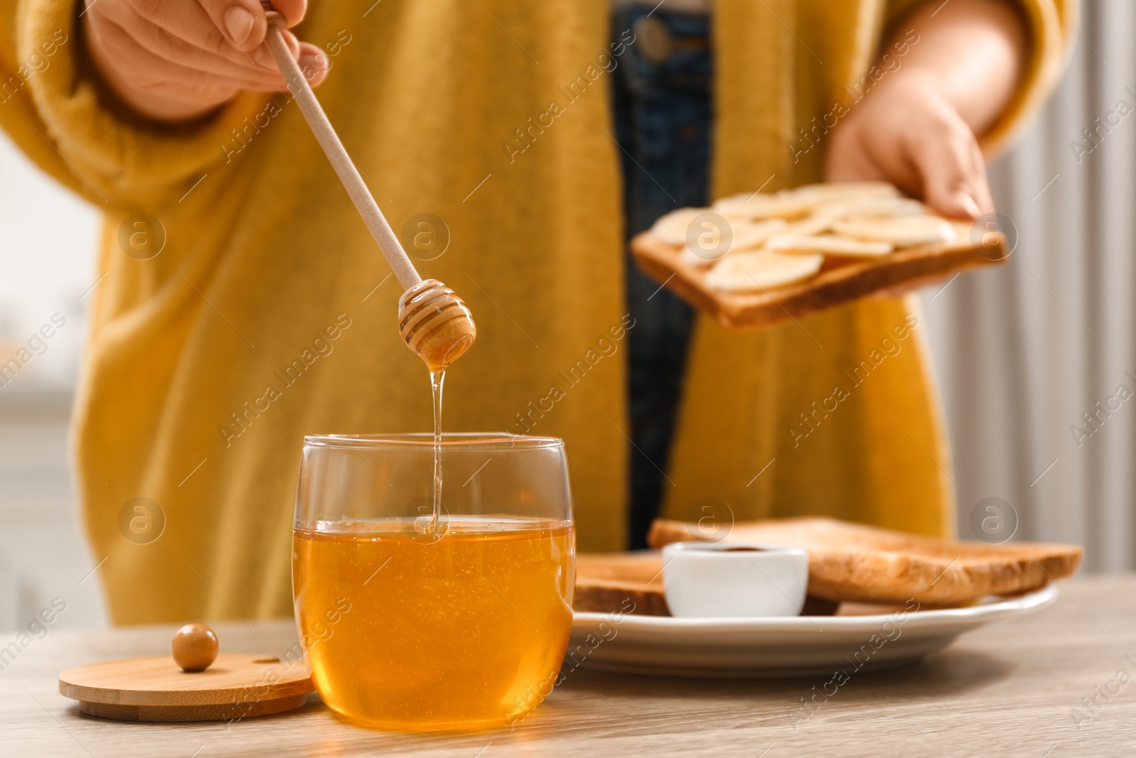 Photo of Woman pouring honey onto toast with banana at table indoors, closeup