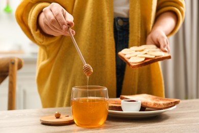 Photo of Woman pouring honey onto toast with banana at table indoors, closeup