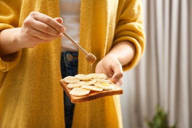 Photo of Woman pouring honey onto toast with banana indoors, closeup