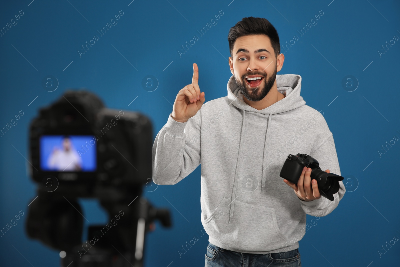 Photo of Young blogger with camera recording video against blue background