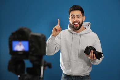 Photo of Young blogger with camera recording video against blue background