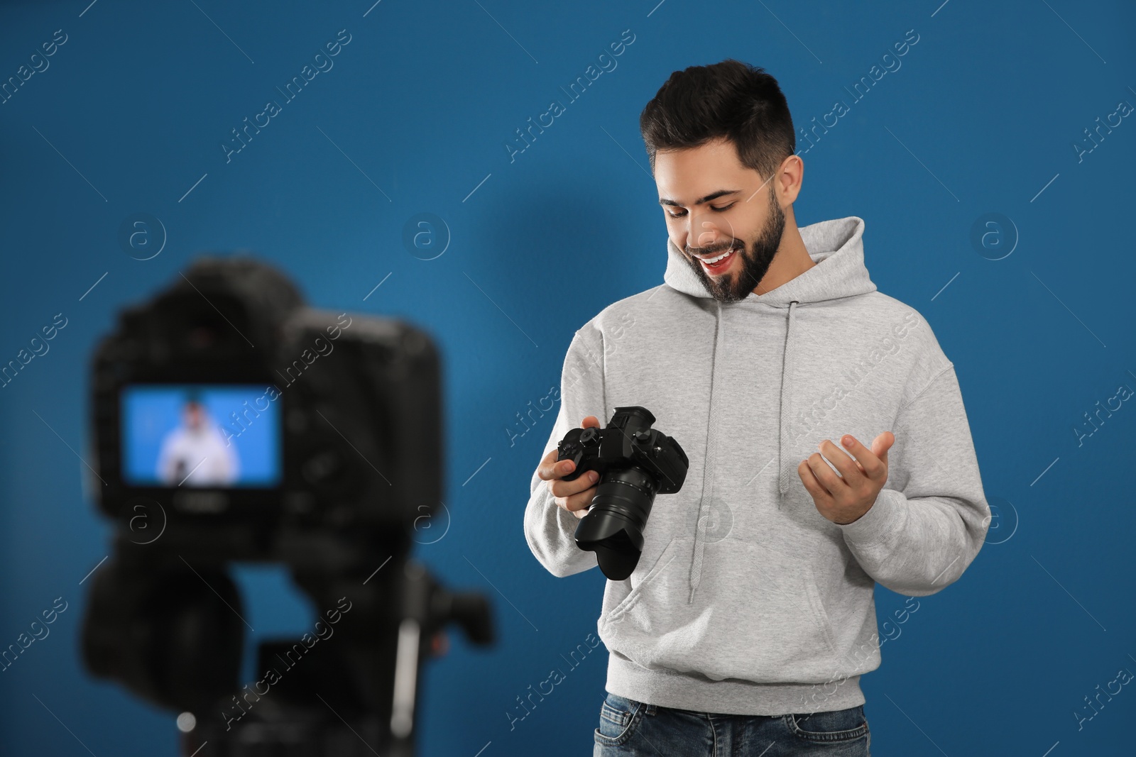 Photo of Young blogger with camera recording video against blue background