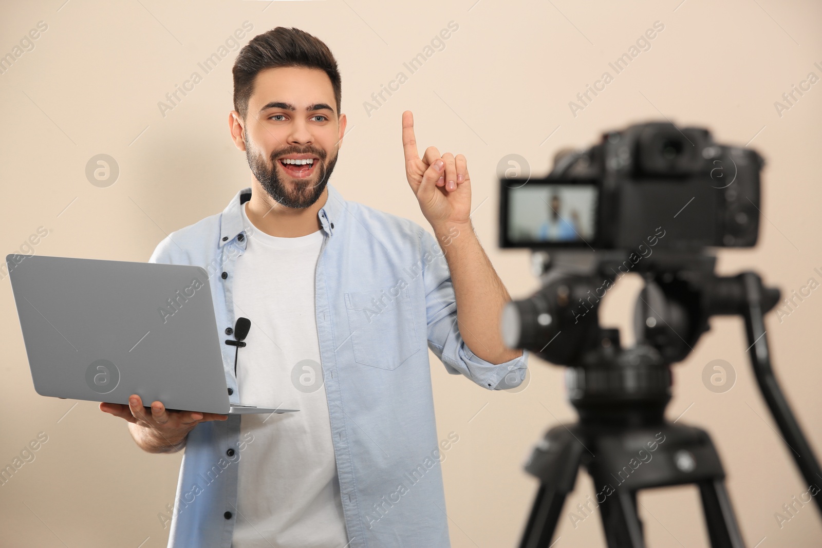 Photo of Young blogger with laptop recording video on camera against beige background