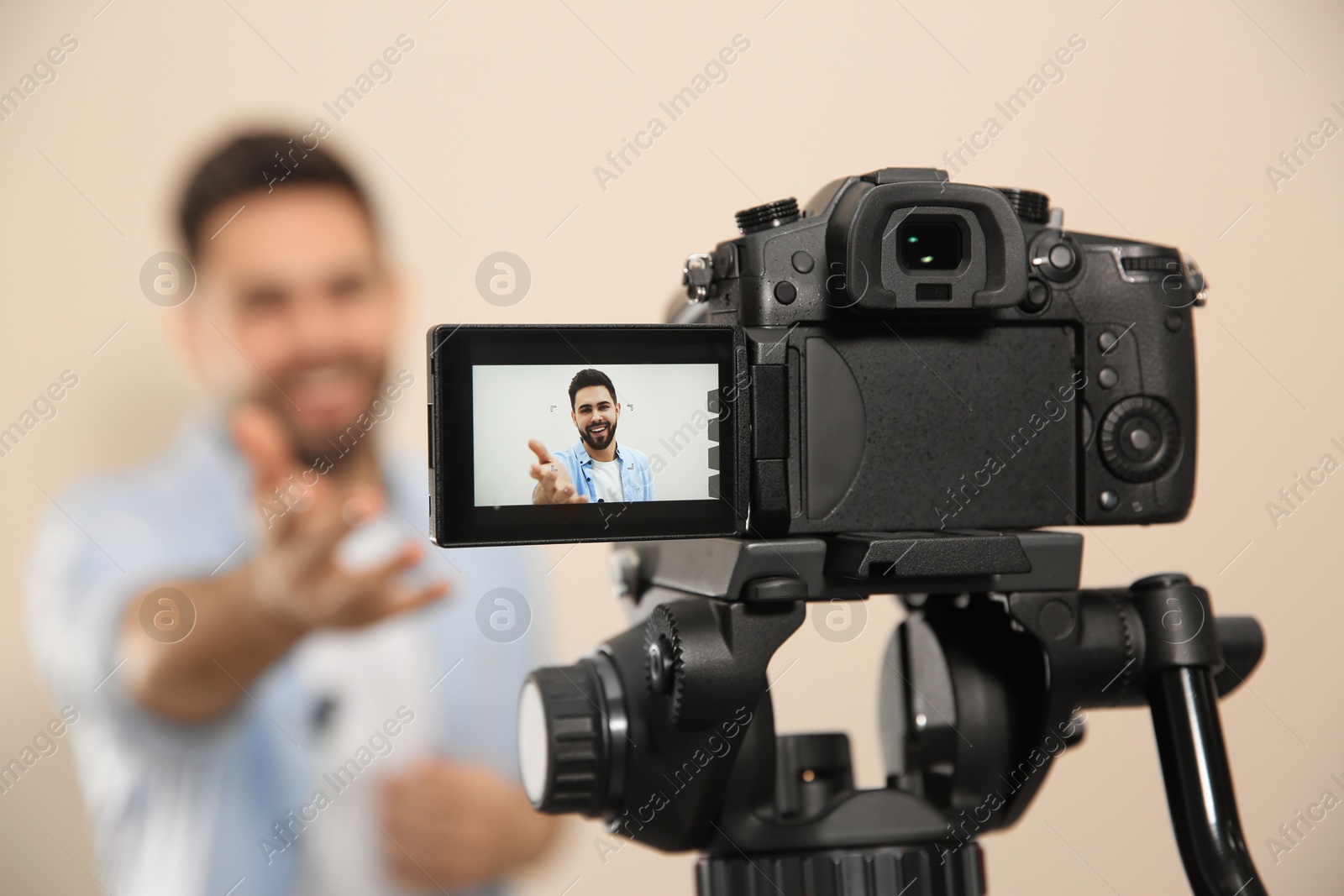 Photo of Young blogger shooting video with camera against beige background, focus on screen