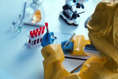Photo of Scientist in chemical protective suit working with blood samples at laboratory, closeup. Virus research