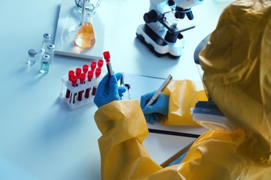 Scientist in chemical protective suit working with blood samples at laboratory, closeup. Virus research