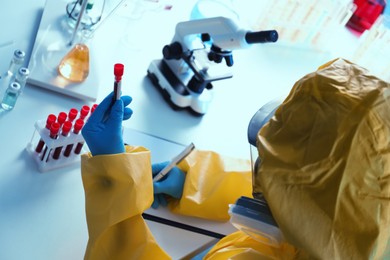 Scientist in chemical protective suit working with blood samples at laboratory, closeup. Virus research