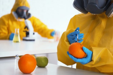 Photo of Scientist in chemical protective suit injecting orange at laboratory, closeup