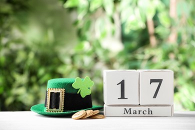 Photo of Composition with block calendar on white wooden table against blurred greenery. St. Patrick's Day celebration