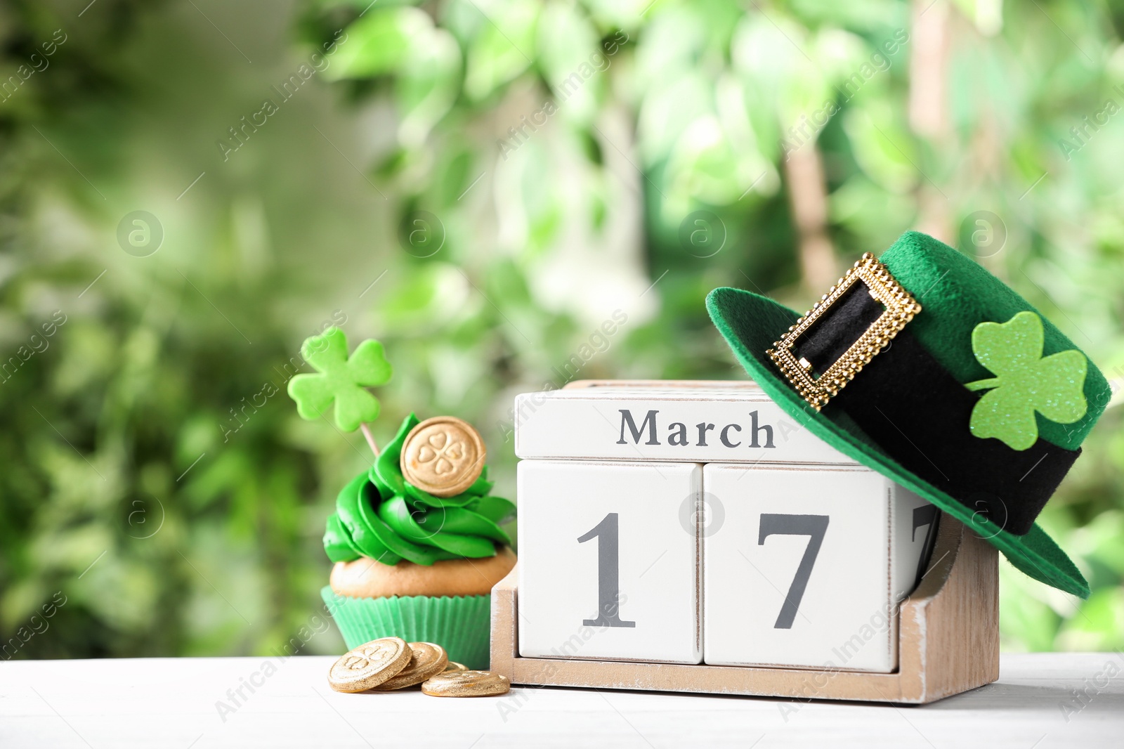 Photo of Composition with block calendar on white wooden table against blurred greenery, space for text. St. Patrick's Day celebration