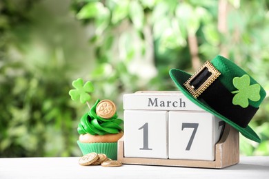 Photo of Composition with block calendar on white wooden table against blurred greenery, space for text. St. Patrick's Day celebration