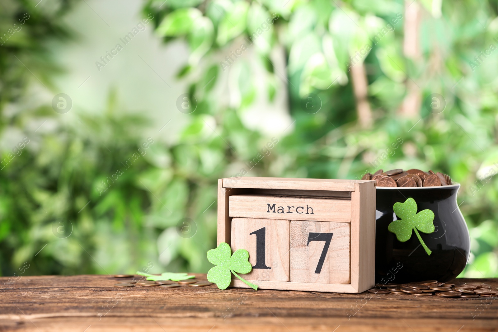 Photo of Composition with block calendar on wooden table against blurred greenery, space for text. St. Patrick's Day celebration