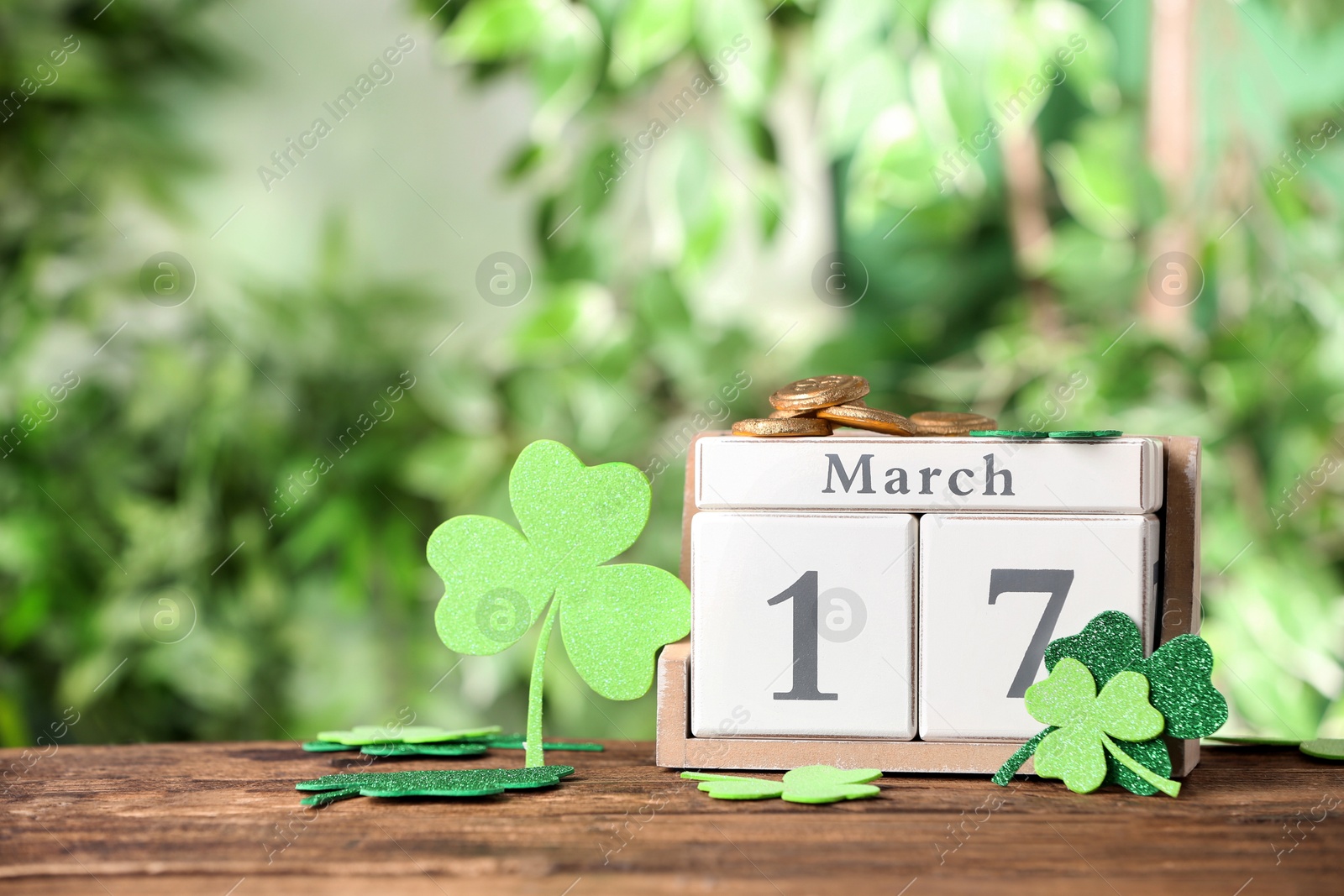 Photo of Composition with block calendar on wooden table against blurred greenery, space for text. St. Patrick's Day celebration