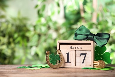 Photo of Composition with block calendar on wooden table against blurred greenery, space for text. St. Patrick's Day celebration