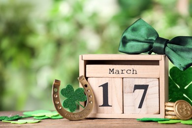 Photo of Composition with block calendar on wooden table against blurred greenery, space for text. St. Patrick's Day celebration