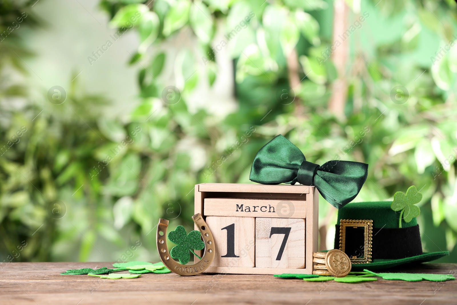 Photo of Composition with block calendar on wooden table against blurred greenery, space for text. St. Patrick's Day celebration