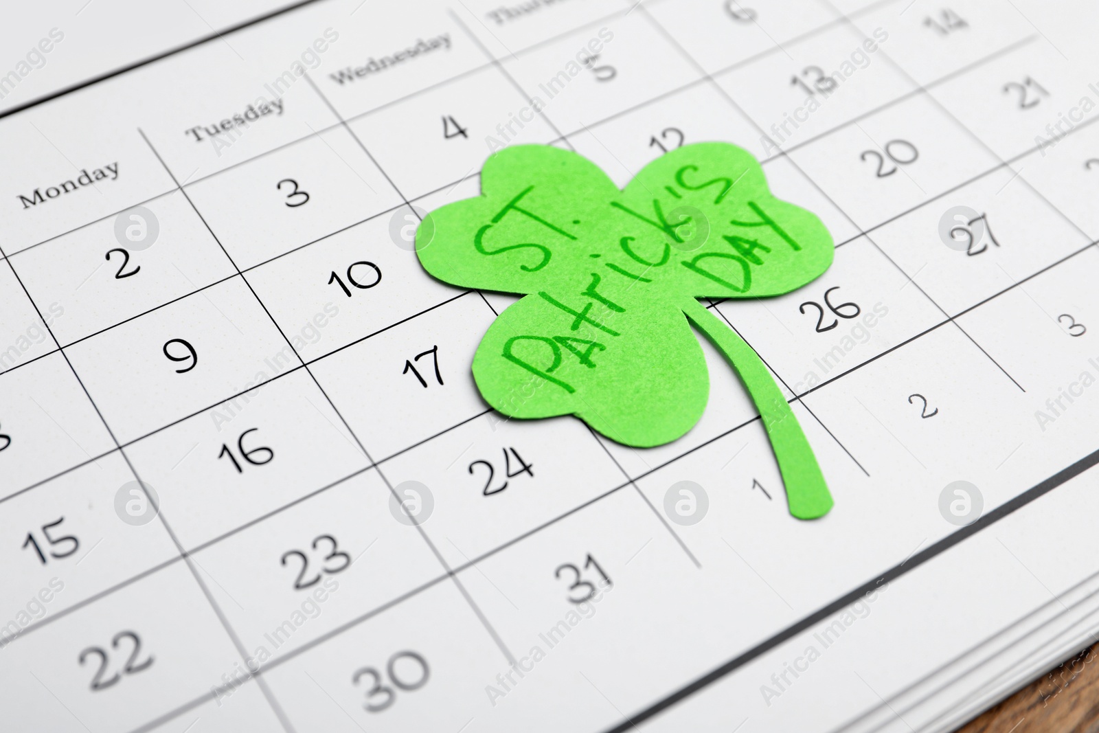 Photo of Paper clover leaf with words ST. PATRICK'S DAY and calendar on wooden background