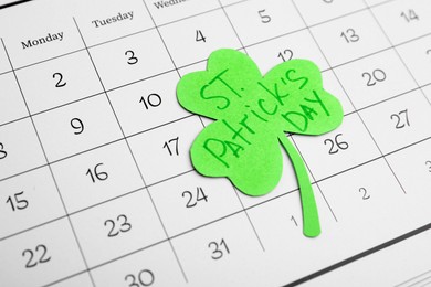 Photo of Paper clover leaf with words ST. PATRICK'S DAY on calendar as background