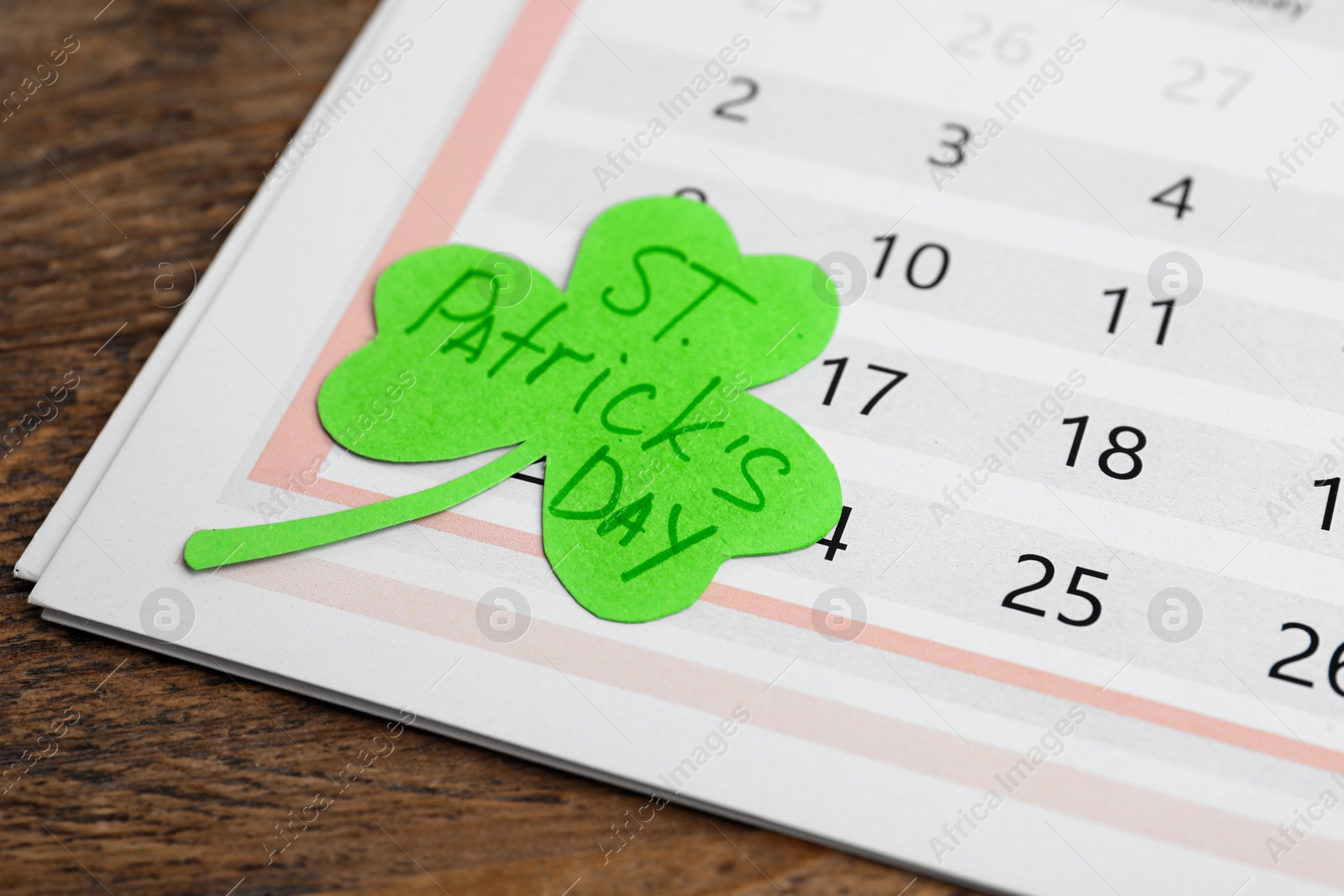 Photo of Paper clover leaf with words ST. PATRICK'S DAY and calendar on wooden background