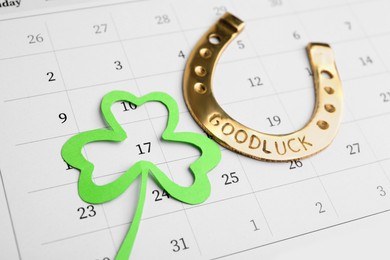 Photo of 17th March marked with paper clover leaf and golden horseshoe on calendar. St. Patrick's Day celebration