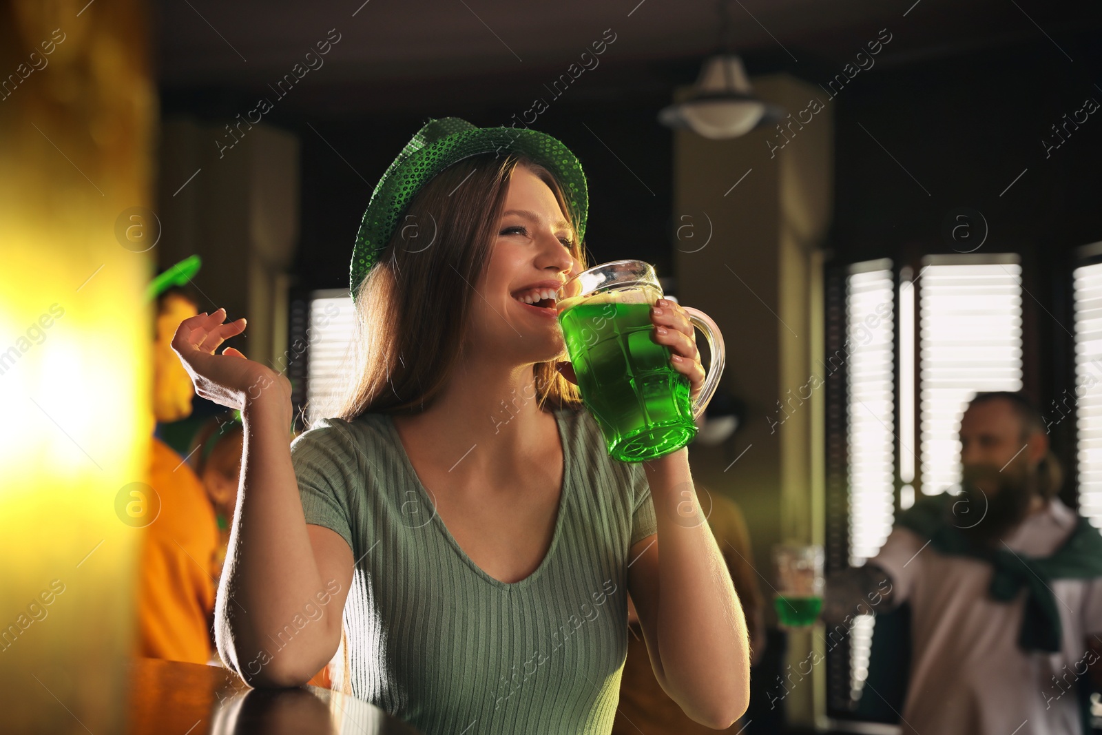 Photo of Young woman drinking green beer in pub. St. Patrick's Day celebration