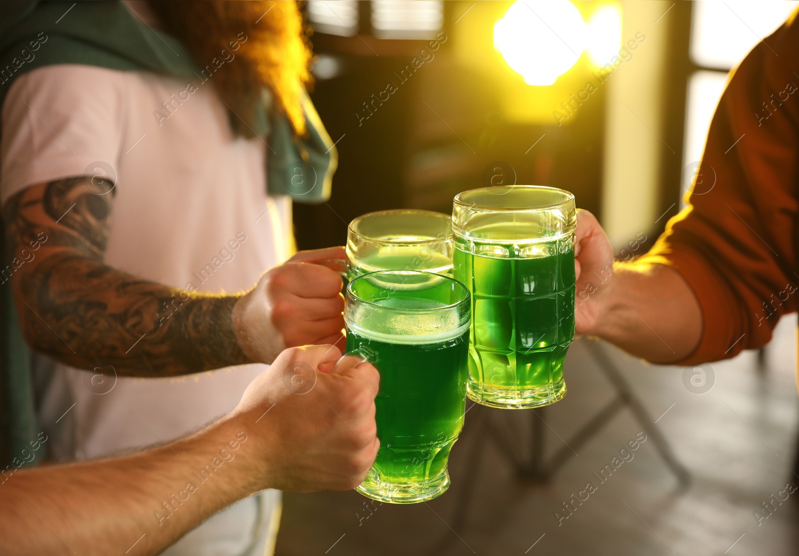 Photo of Group of friends toasting with green beer in pub, closeup. St. Patrick's Day celebration