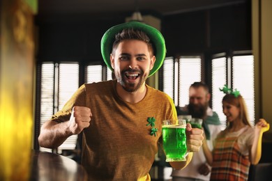 Photo of Happy young man with glass of green beer in pub. St. Patrick's Day celebration