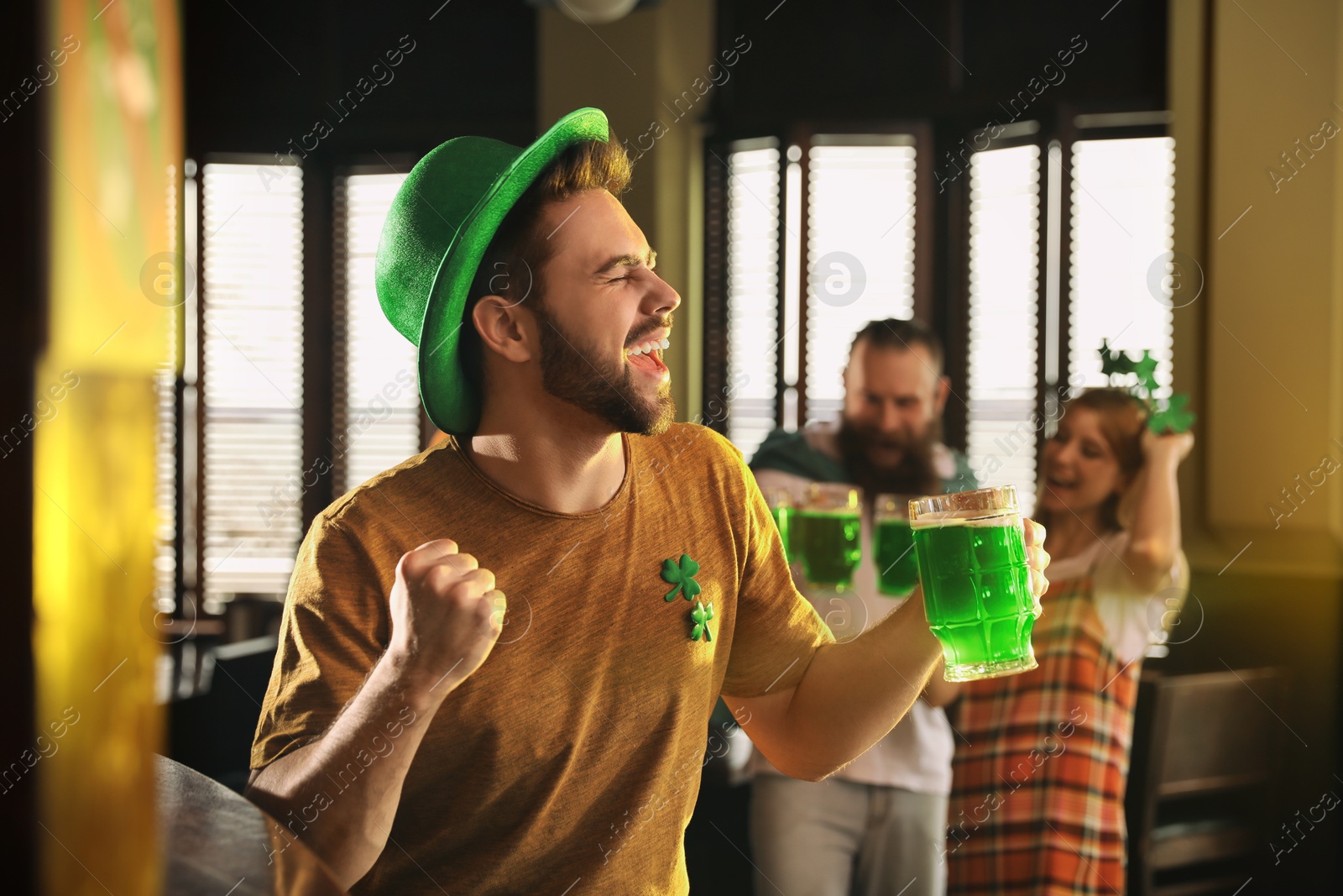 Photo of Emotional young man with glass of green beer in pub. St. Patrick's Day celebration