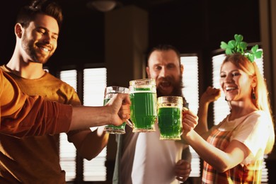 Photo of Group of friends toasting with green beer in pub, focus on hands. St. Patrick's Day celebration