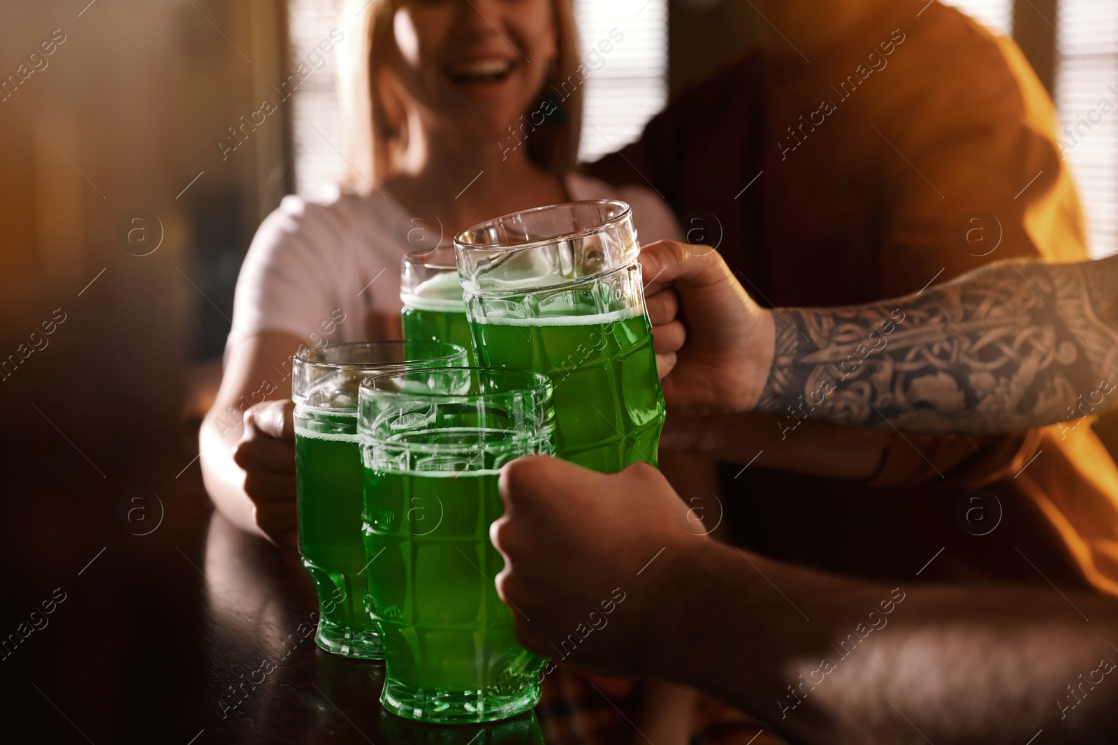 Photo of Group of friends toasting with green beer in pub, closeup. St. Patrick's Day celebration