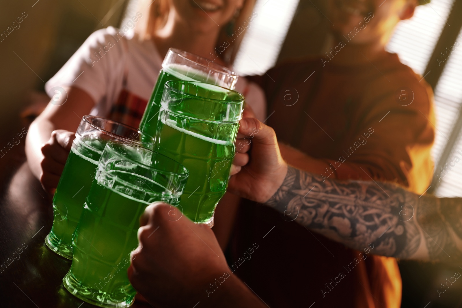 Photo of Group of friends toasting with green beer in pub, closeup. St. Patrick's Day celebration