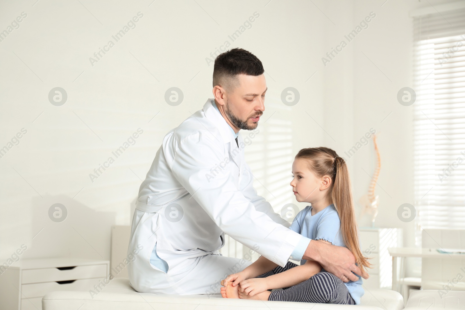 Photo of Professional orthopedist examining little girl in clinic