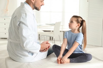 Photo of Professional orthopedist examining little girl in clinic