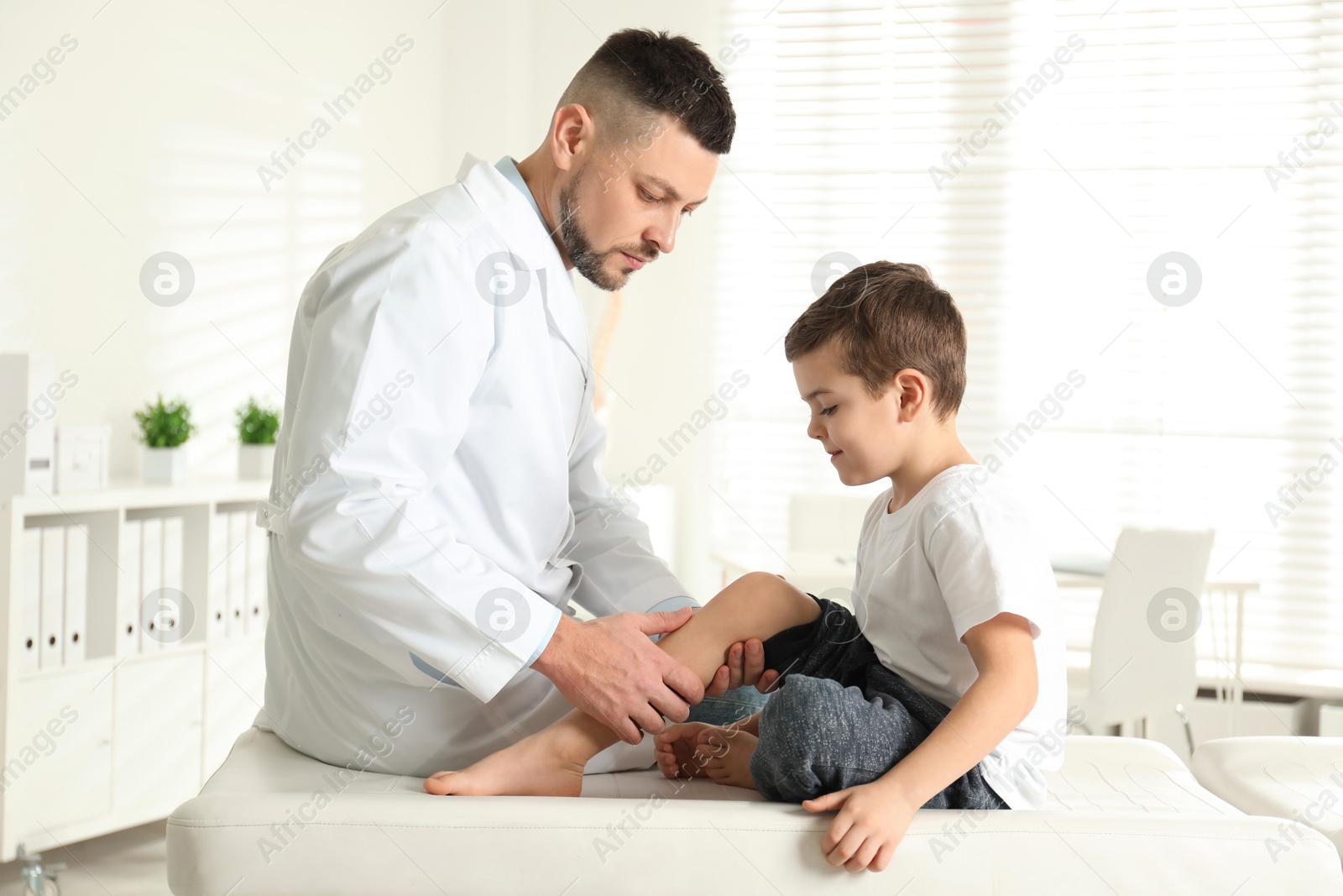 Photo of Professional orthopedist examining little patient's leg in clinic