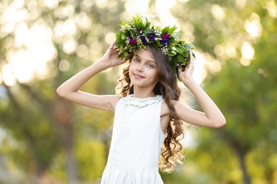 Photo of Cute little girl wearing wreath made of beautiful flowers outdoors on sunny day