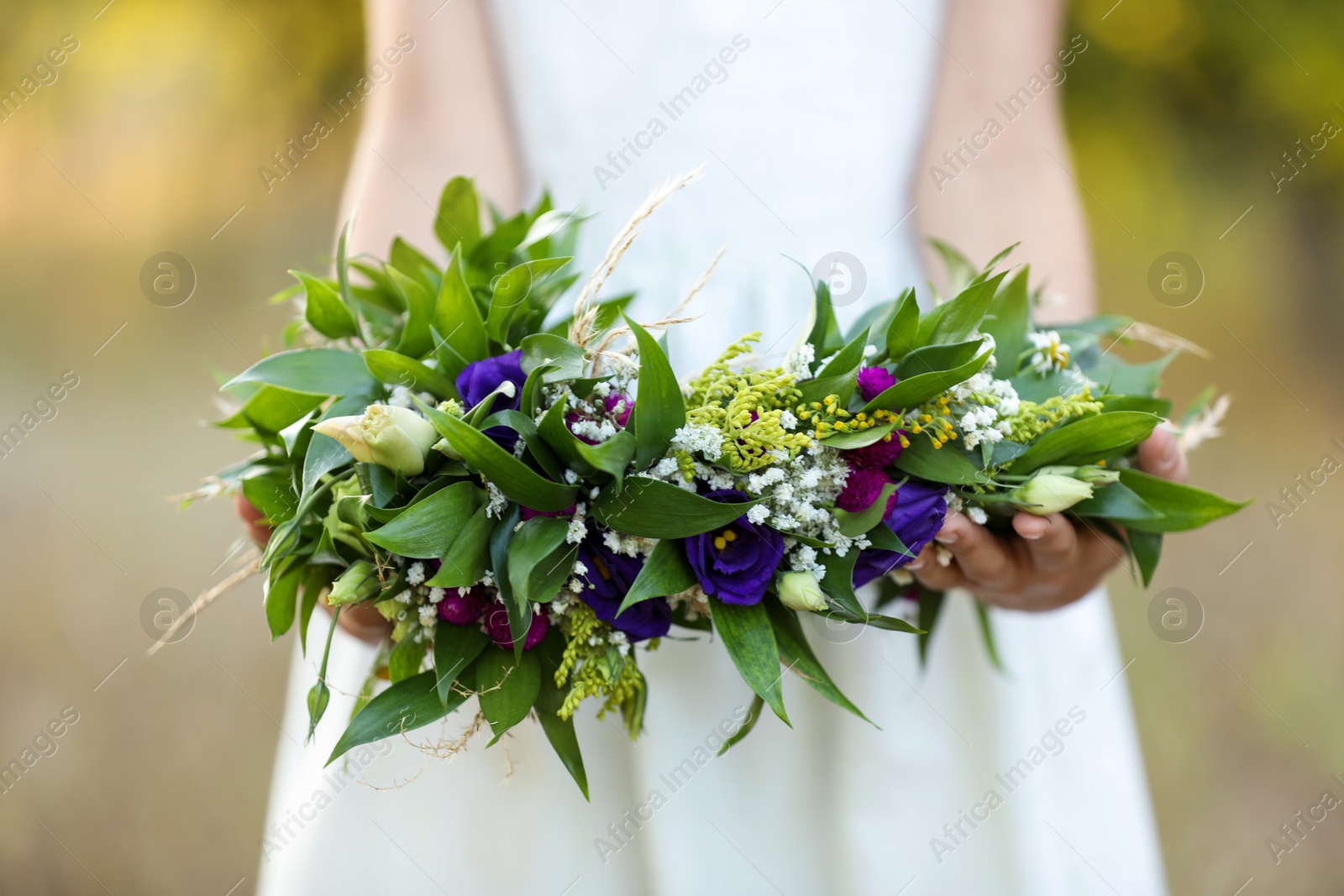 Photo of Little girl holding wreath made of beautiful flowers outdoors on sunny day, closeup