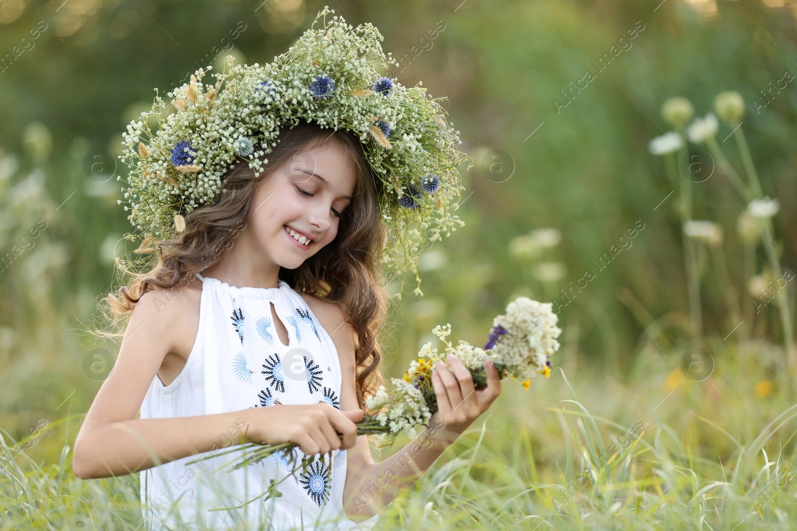 Photo of Cute little girl wearing wreath made of beautiful flowers in field