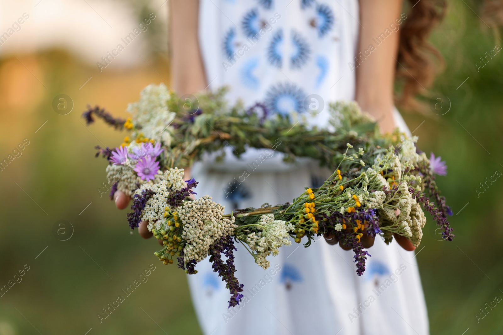 Photo of Little girl holding wreath made of beautiful flowers outdoors, closeup