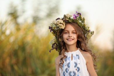 Photo of Happy little girl wearing wreath made of beautiful flowers outdoors