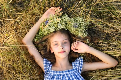 Photo of Cute little girl wearing wreath made of beautiful flowers on green grass, top view