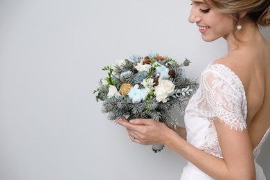 Beautiful bride with winter wedding bouquet on light grey background. Space for text