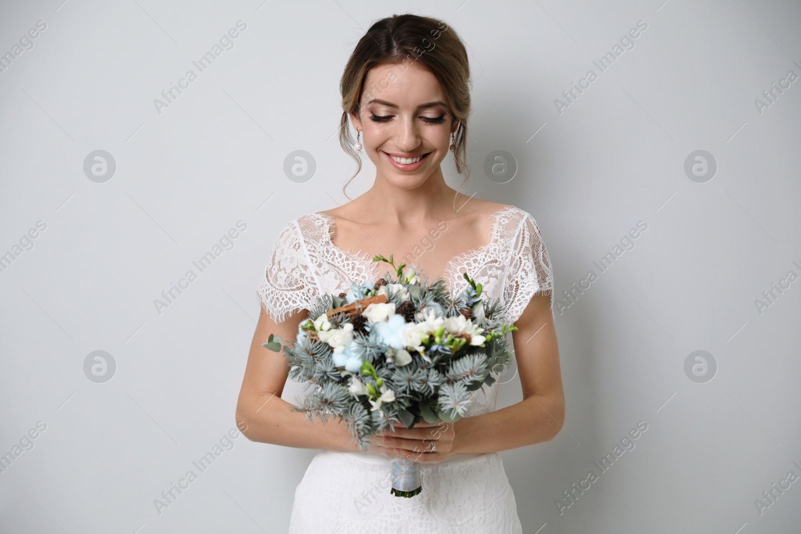 Photo of Beautiful bride with winter wedding bouquet on light grey background