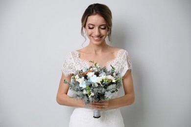 Beautiful bride with winter wedding bouquet on light grey background