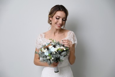 Beautiful bride with winter wedding bouquet on light grey background