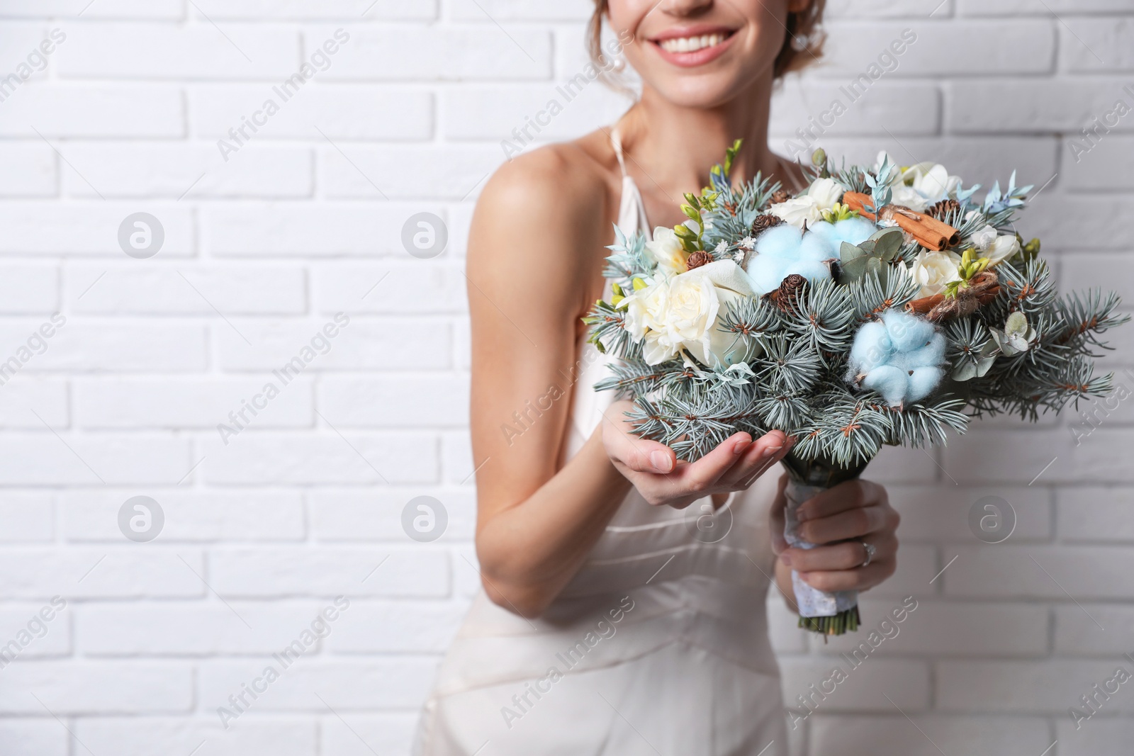 Photo of Beautiful bride with winter wedding bouquet near white brick wall, closeup. Space for text