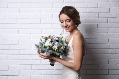 Beautiful bride with winter wedding bouquet near white brick wall