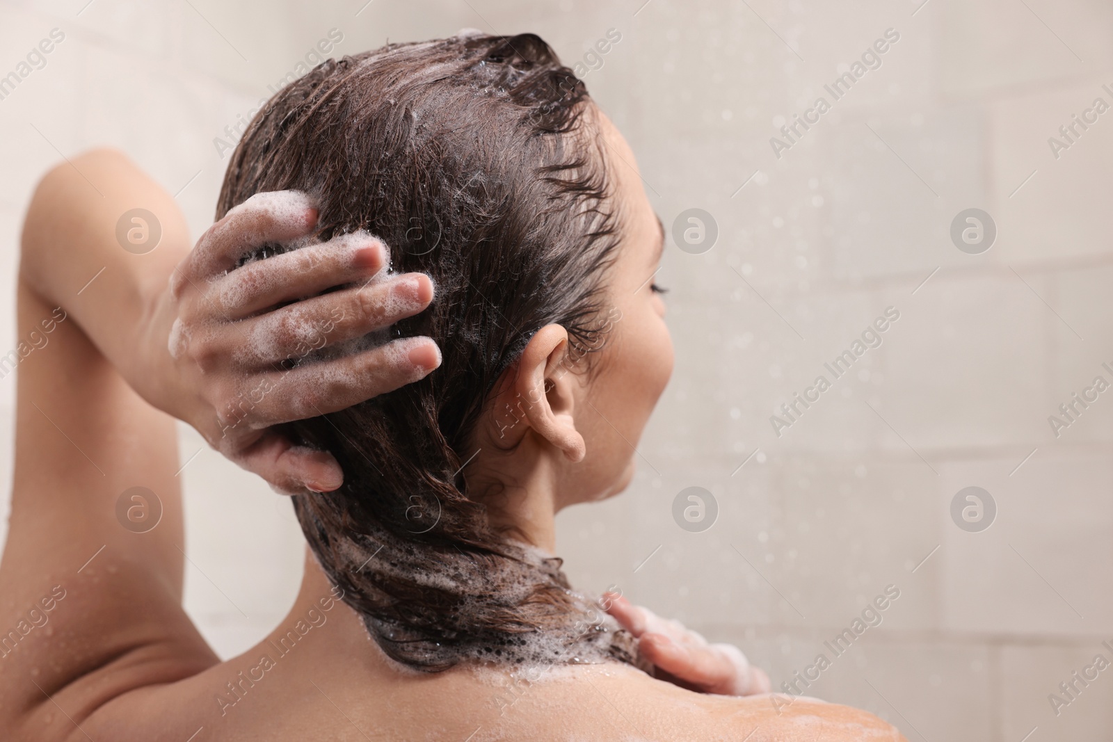 Photo of Woman washing hair while taking shower at home, back view