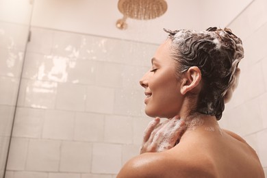 Photo of Young woman washing hair while taking shower at home. Space for text